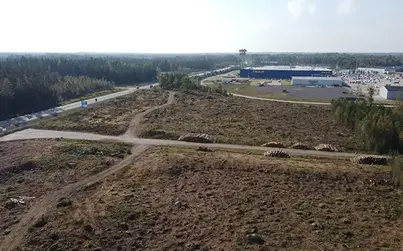 Drönarbild på tom mark med skog och en IKEA-byggnad i bakgrunden.