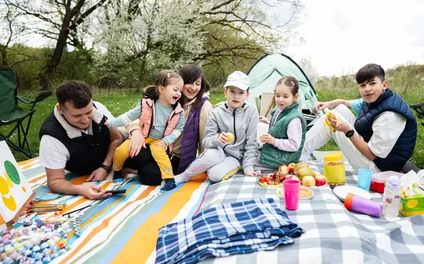 Familj på picknick med ängar och ett blommande träd i bakgrunden.