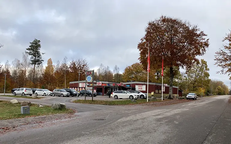 En ICA-butik med en parkering med ett flertal bilar och träd omkring en höstdag med grå himmel.