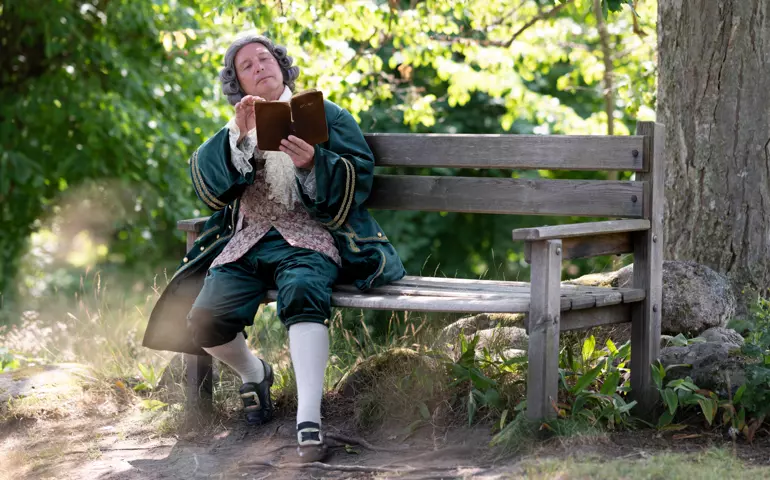 Carl von Linne sitter på en bänk och läser en bok