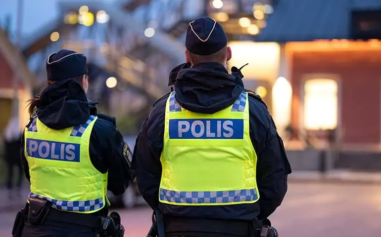 En manlig och en kvinnlig polis står vid tågstationen i Älmhult. De har gula västar på sig, på ryggen står det polis. 