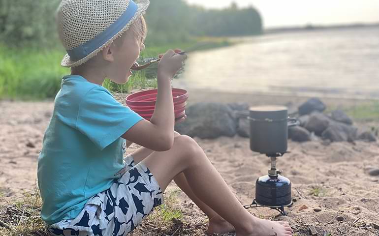 ett barn sitter vid en sjö och äter mat 