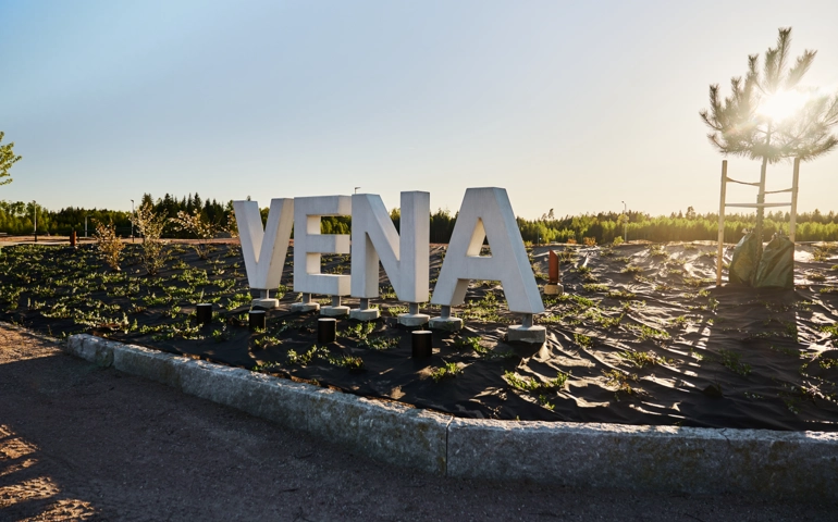 vita stora bokstäver som bildar namnet Vena, som är ett område i västra Älmhult. I bakgrunden håller solen på att gå ner och skapar ett härligt ljus.