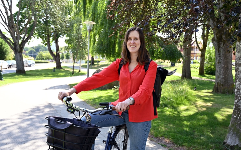 Lovisa Thorneman sitter på en cykel och har ena benet i marken. Hon har ryggsäck och ler mot kameran. I bakgrunden syns Björkparken.