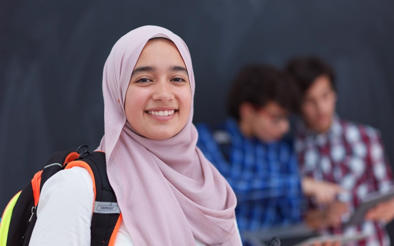 En ung kvinna i hijab ler mot kameran. Hon har en ryggsäck över axeln.