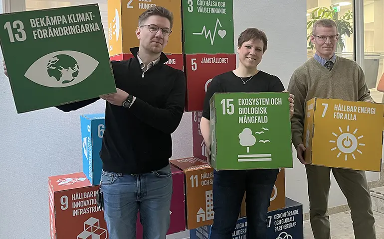 Tre personer håller upp kuber med måltexter och ikoner om miljön.