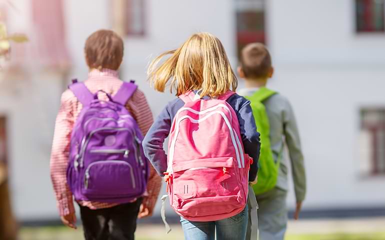 Barn med ryggsäckar går mot skolan