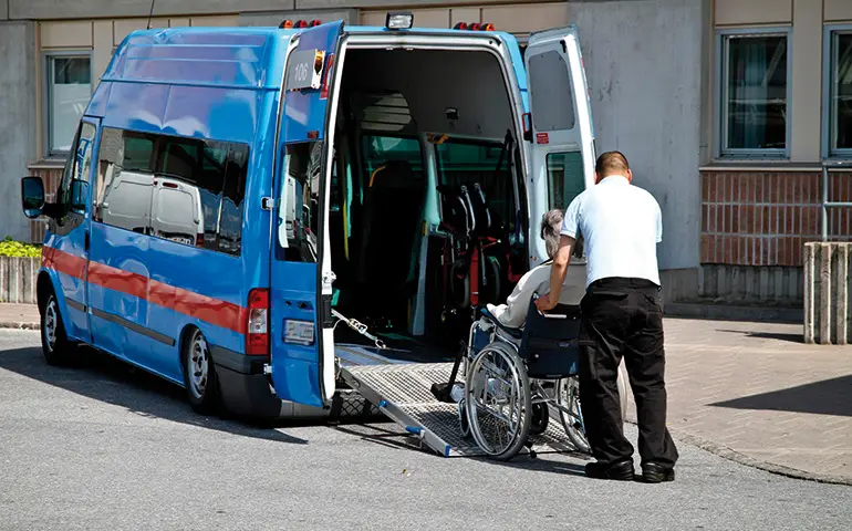 En man hjälper en person i rullstol in i en minibuss.