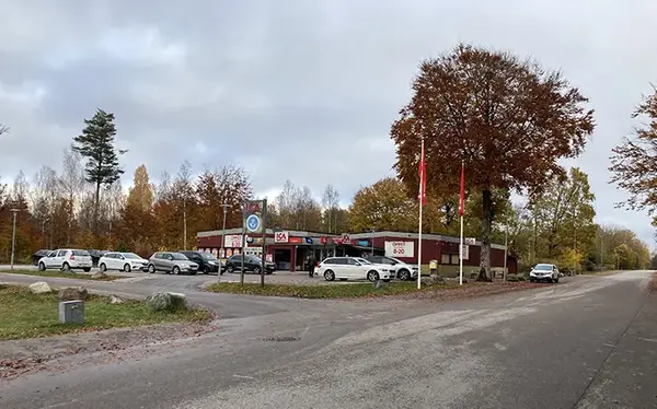 En ICA-butik med en parkering med ett flertal bilar och träd omkring en höstdag med grå himmel.