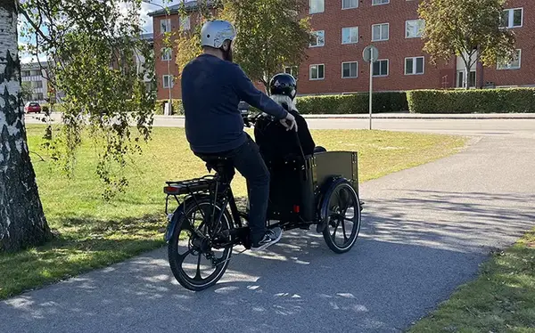 En person som cyklar på en cargobike med en person som åker med.