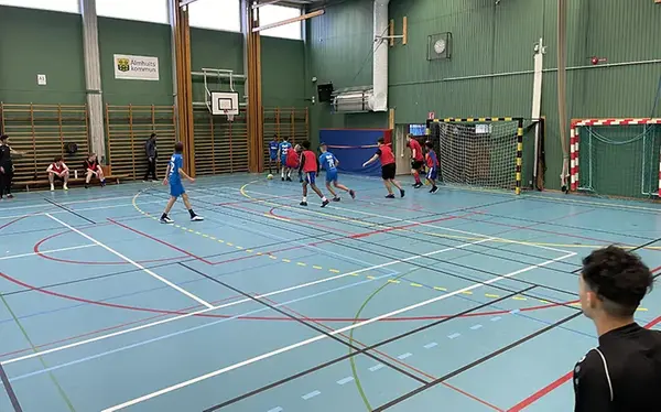 Ett tiotal ungdomar spelar fotboll i en idrottshall.