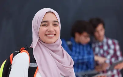 En ung kvinna i hijab ler mot kameran. Hon har en ryggsäck över axeln.