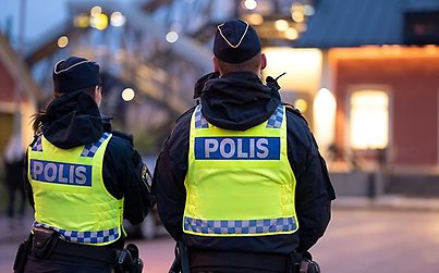 En manlig och en kvinnlig polis står vid tågstationen i Älmhult. De har gula västar på sig, på ryggen står det polis. 