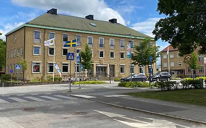 Gul tegelbyggnad med flaggor och en kullerstensbelagd gata framför. Blå himmel. 